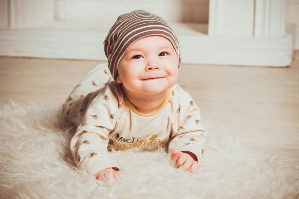 Charming baby smiling while lying indoors on soft rug wearing cozy outfit.